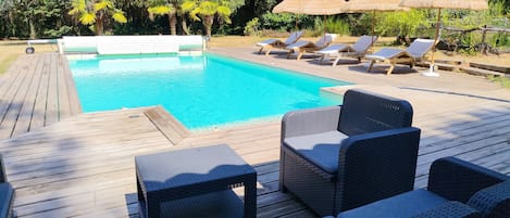 Ett trädäck med en pool, solstolar och parasoller.