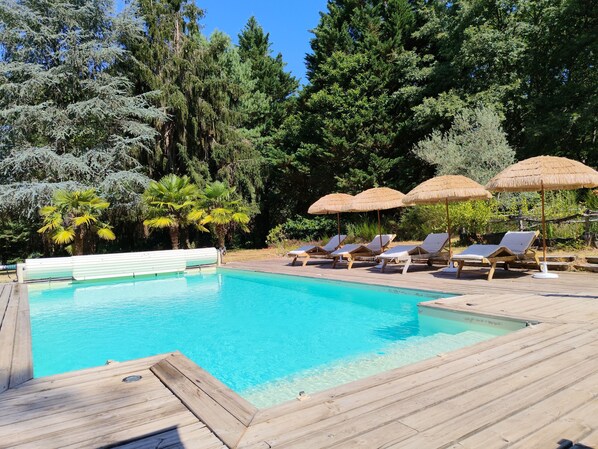 A pool with clear water, surrounded by wooden deck and lounge chairs.