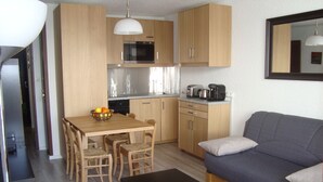 A compact living space with a kitchenette, a dining area with a table and chairs, a sofa, and a small black table. - Studio accredits 3clés the slopes Centre station free wifi (Les Deux-Alpes)