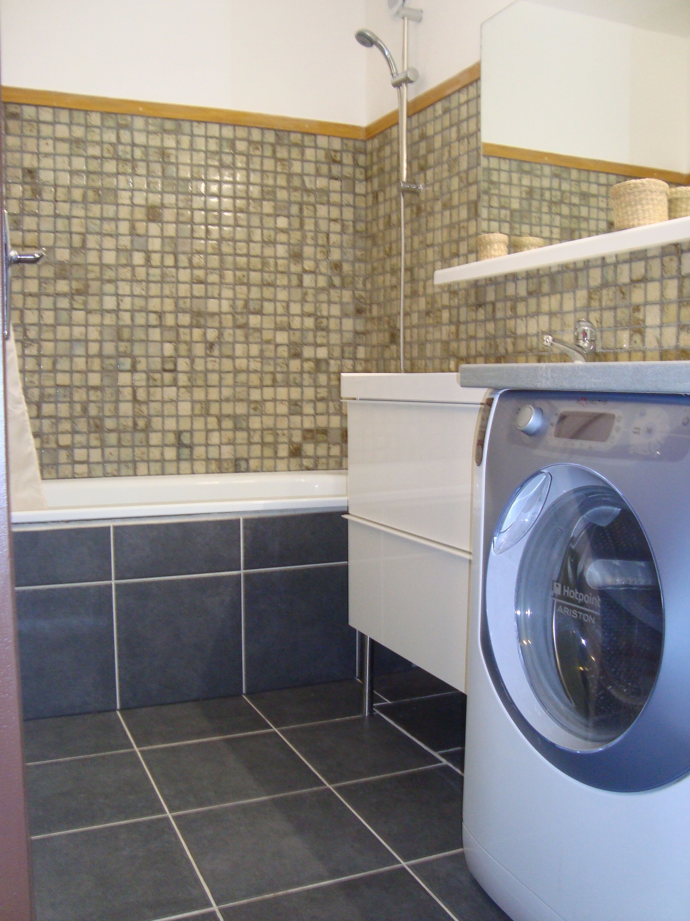 A compact laundry room with a washing machine, a bathtub, and a tiled shower area.