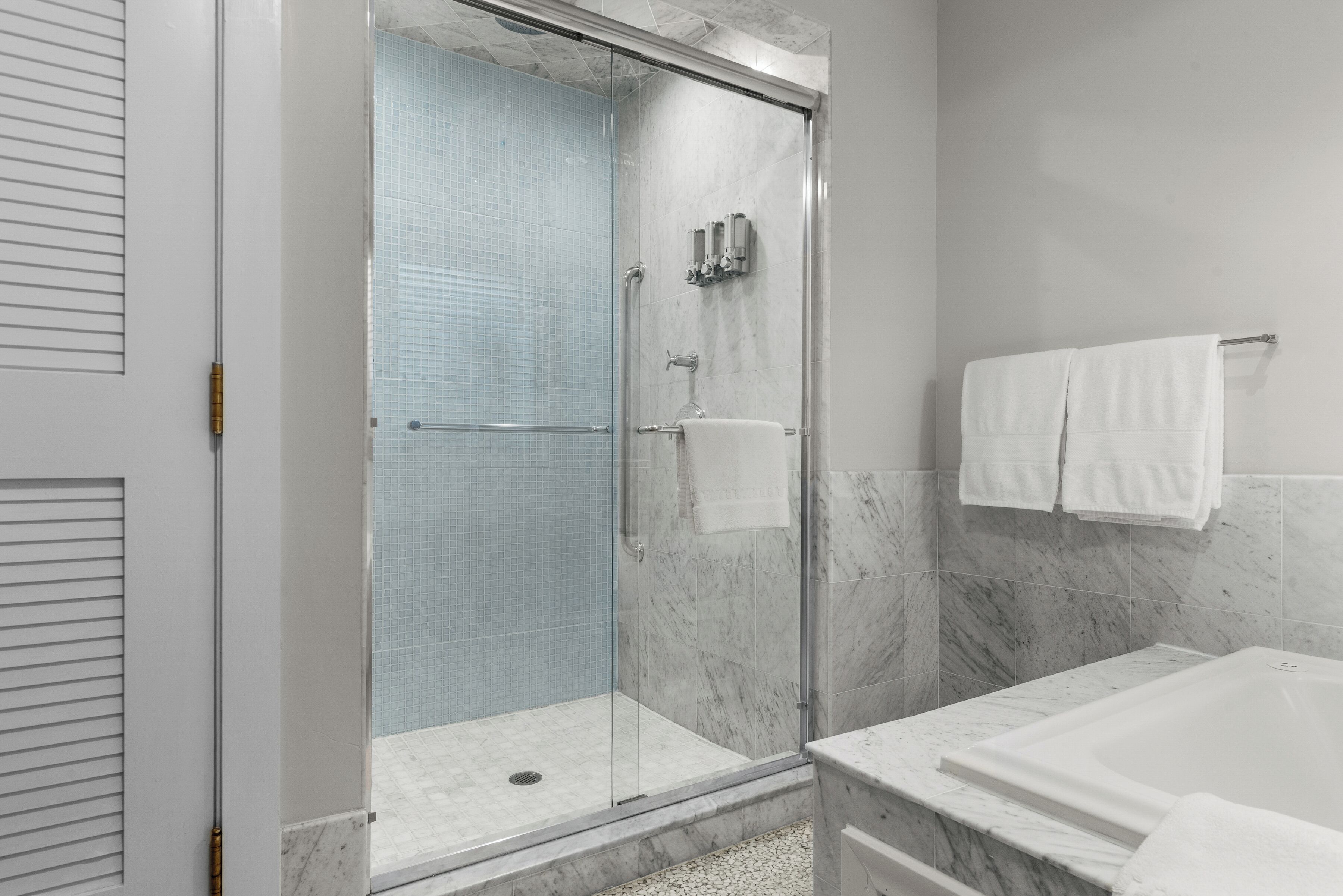 A modern bathroom with a glass-enclosed shower, a marble bathtub, and a white towel rack.