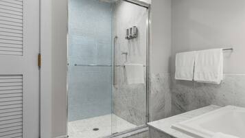 A modern bathroom with a glass-enclosed shower, a marble bathtub, and a white towel rack.