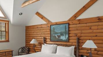 Una camera da letto con soffitto in legno, un letto, un comodino, una lampada, una sedia e un quadro appeso al muro.