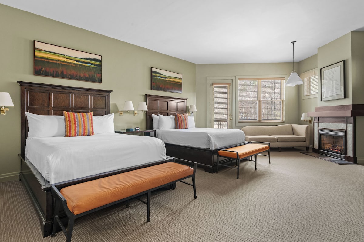 A hotel room with two beds, a sofa, a fireplace, and artwork on the walls.