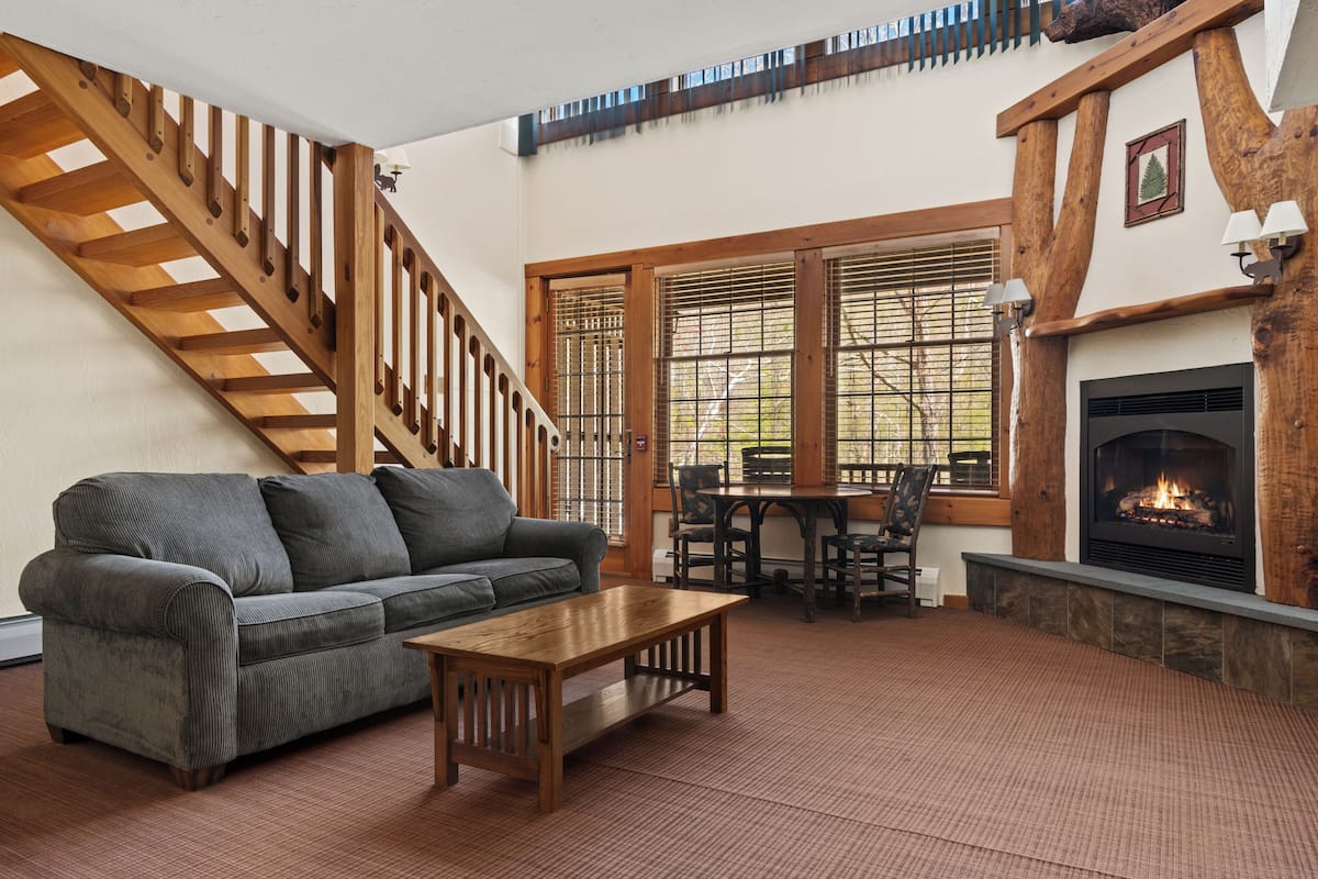 A living room with a sofa, coffee table, fireplace, and a staircase.