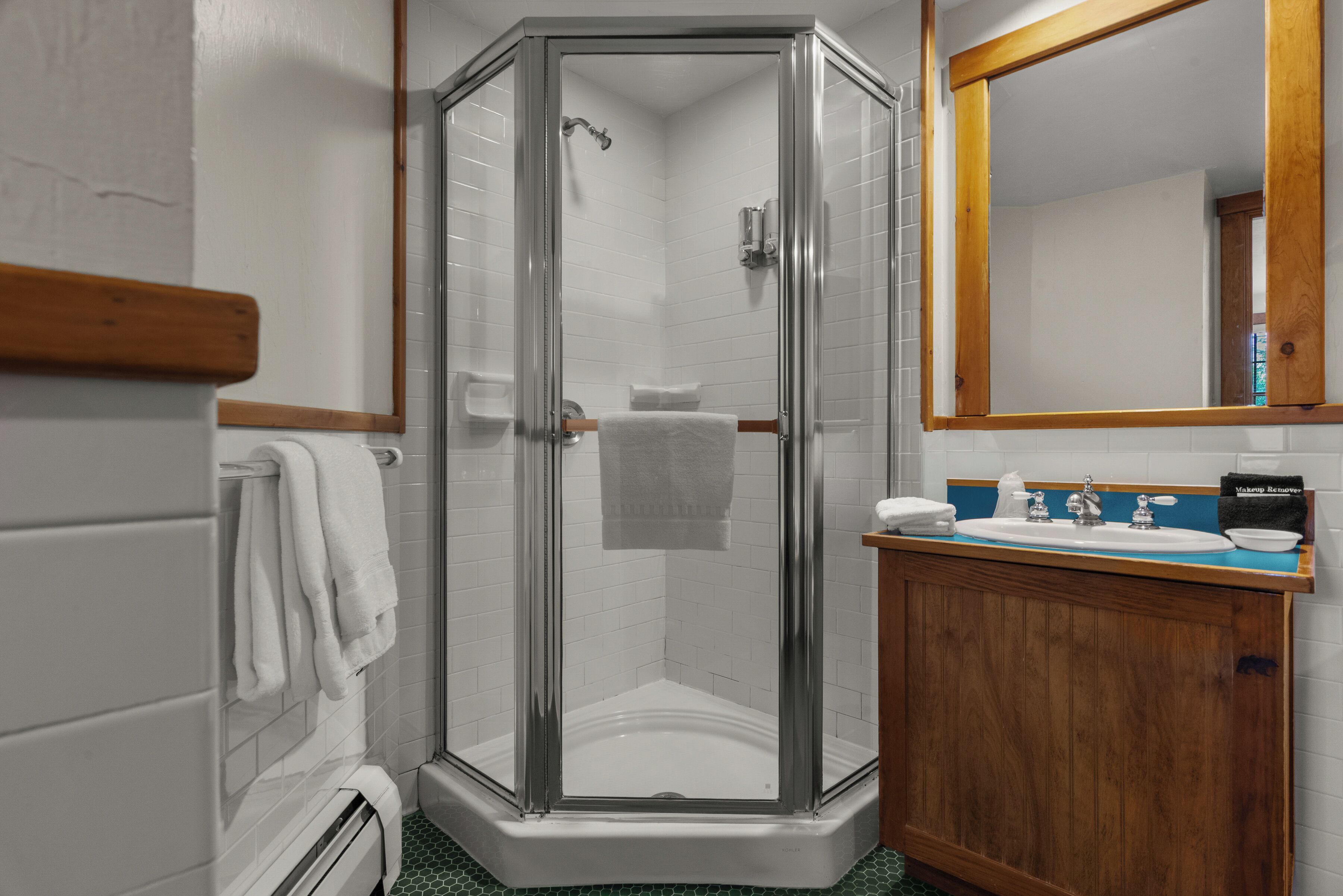 Ducha en esquina con puertas de cristal, tocador de madera con lavamanos y espejo encima.