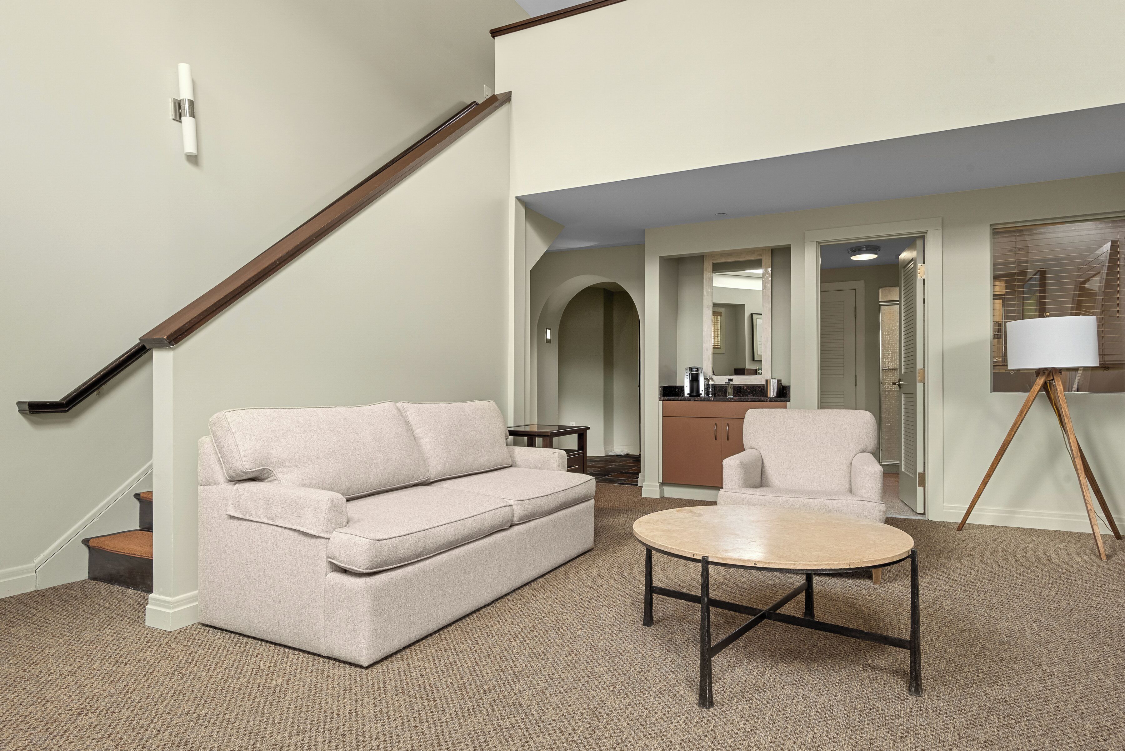 A living room with a sofa, armchair, coffee table, and a lamp.