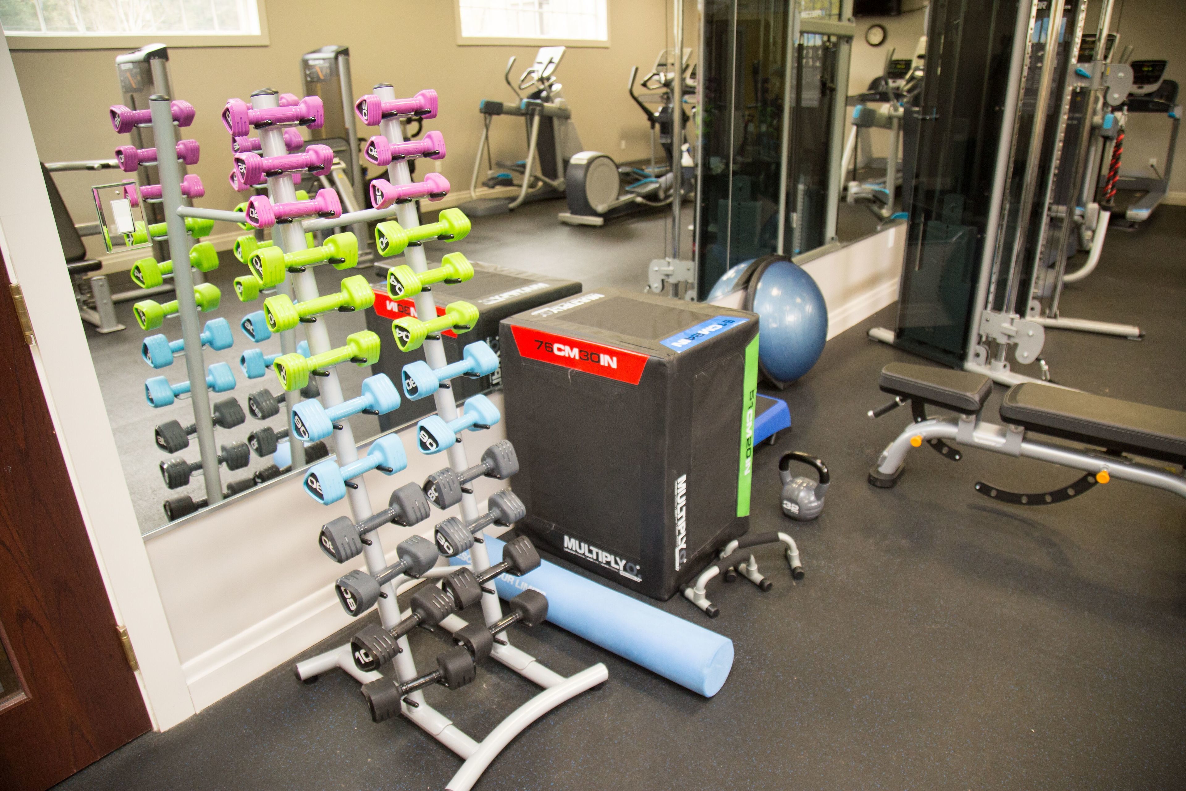 A gym with various exercise equipment, including dumbbells, a weight bench, and cardio machines.