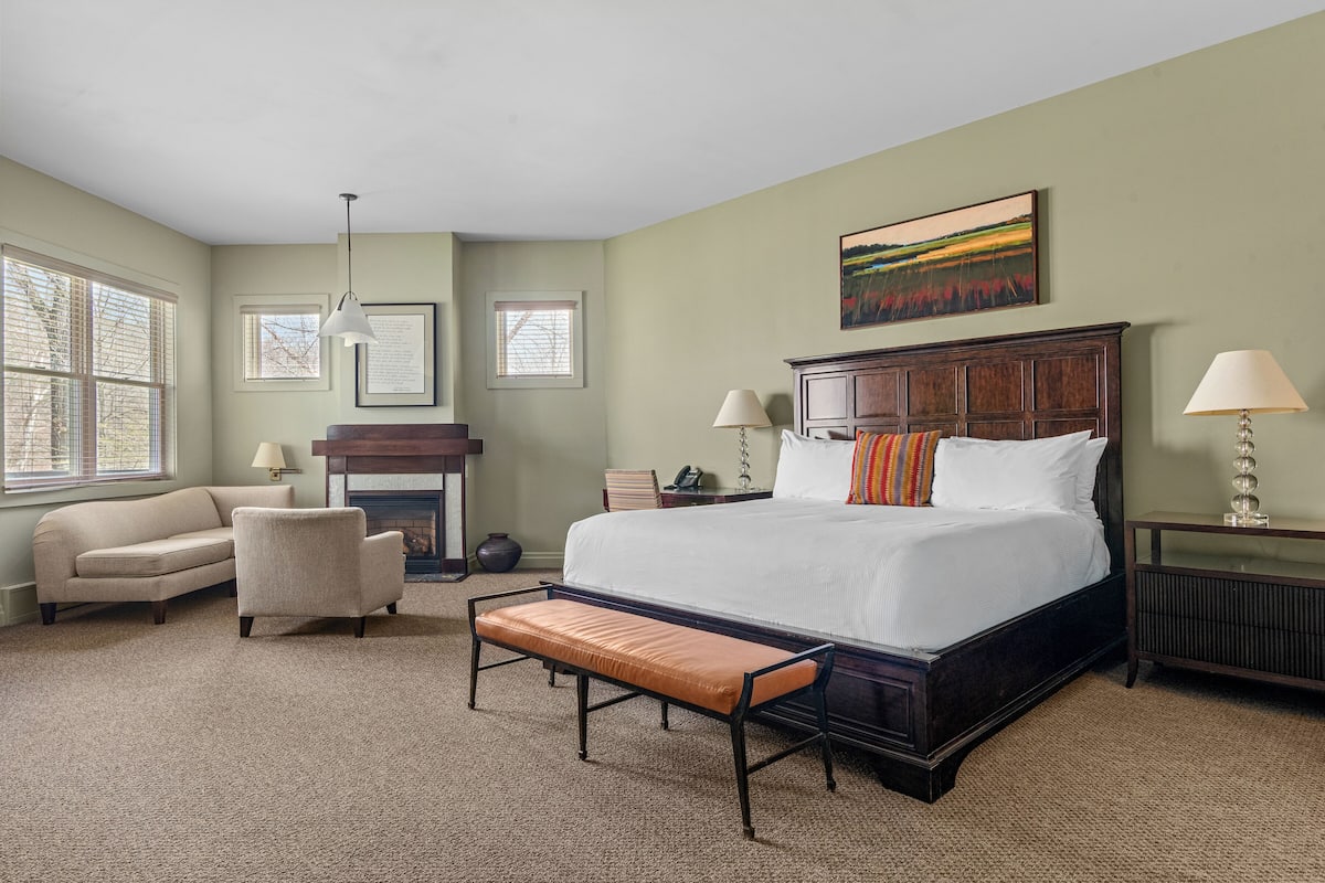 A bedroom with a large bed, a bench, a sofa, and a fireplace.