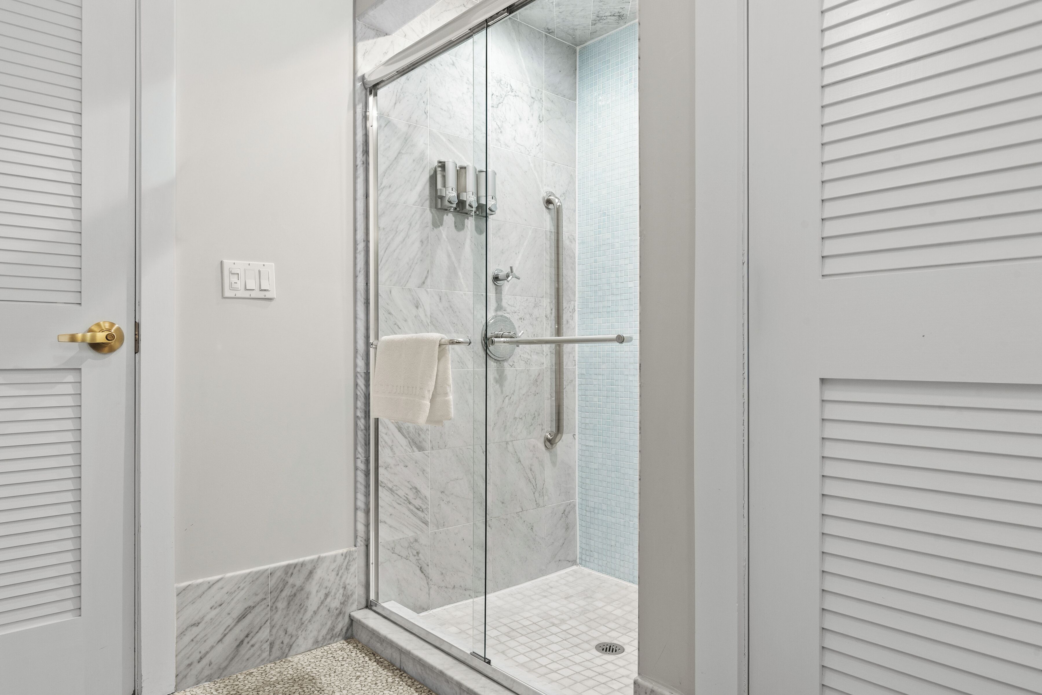 A glass-enclosed shower with a marble wall, a towel rack, and a handrail.