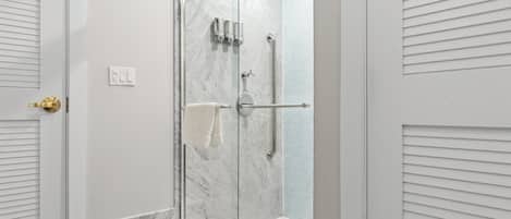 A glass-enclosed shower with a marble wall, a towel rack, and a handrail.