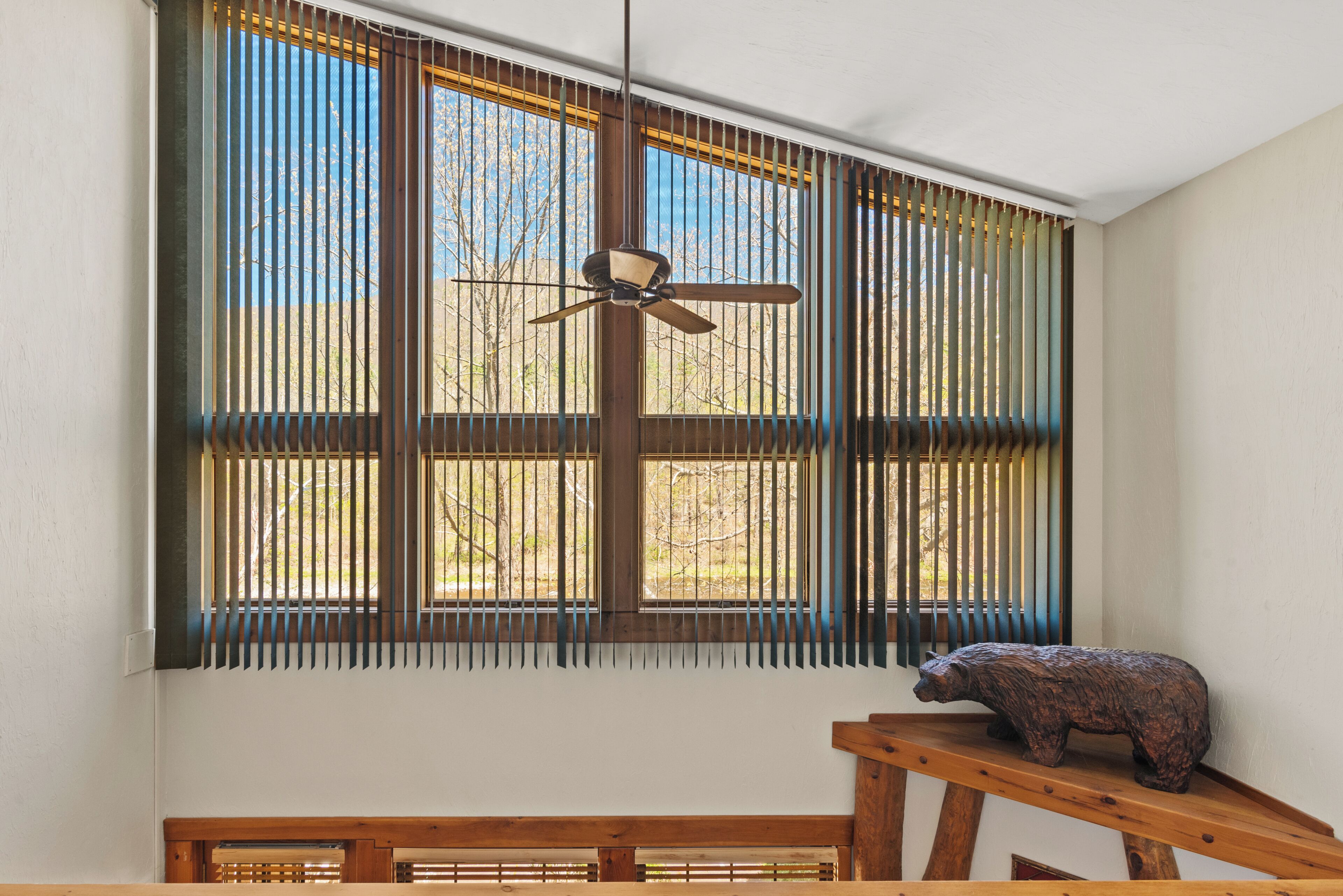 A room with large windows, a ceiling fan, and a wooden bench.