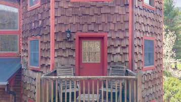 A wooden cabin with a red door, multiple windows, and a balcony with chairs.