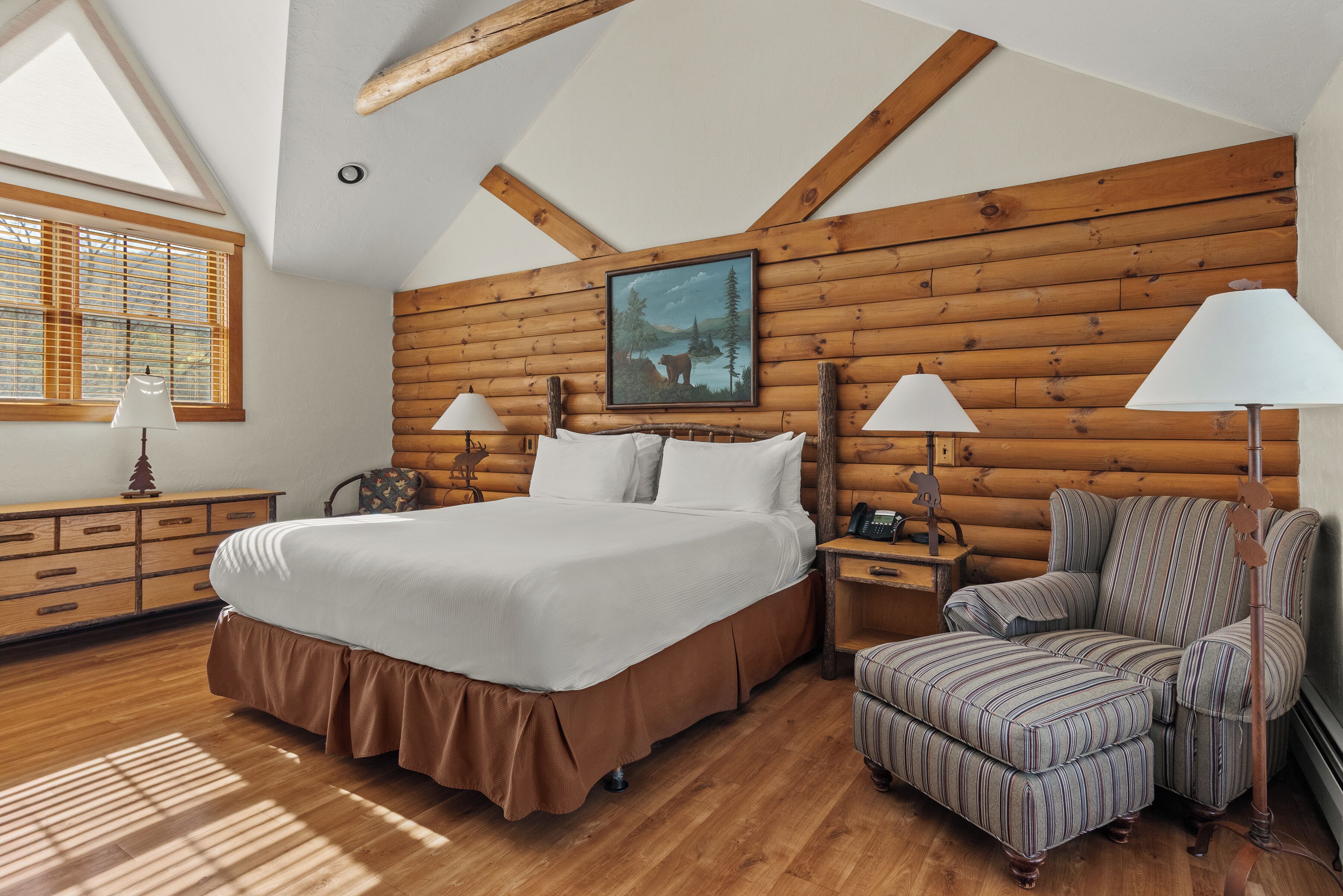 Ein Schlafzimmer mit einem großen Bett, zwei Nachttischen, einem Sessel und einer Holzwand, sowie einem Gemälde.
