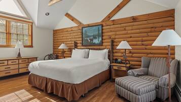 Ein Schlafzimmer mit einem großen Bett, zwei Nachttischen, einem Sessel und einer Holzwand, sowie einem Gemälde.