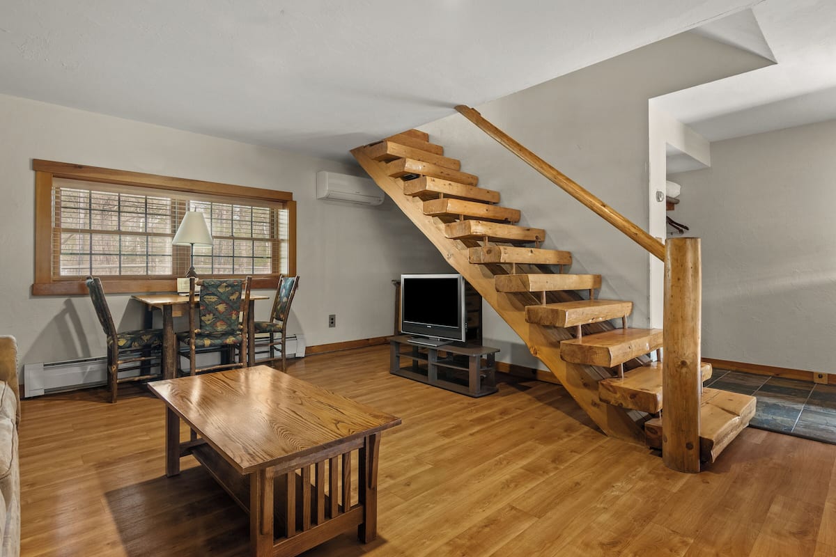 A wooden staircase, a dining table, and a TV in a room with wooden flooring and a window.
