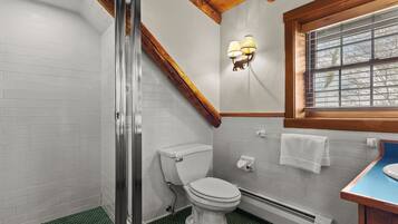 A bathroom with a shower, toilet, and sink, featuring white tiles, a wooden ceiling, and a window.