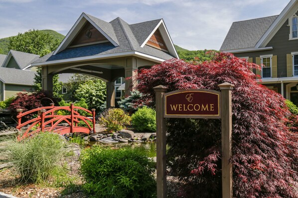 A well-maintained garden with a red bridge, a welcome sign, and a building with a gabled roof.
