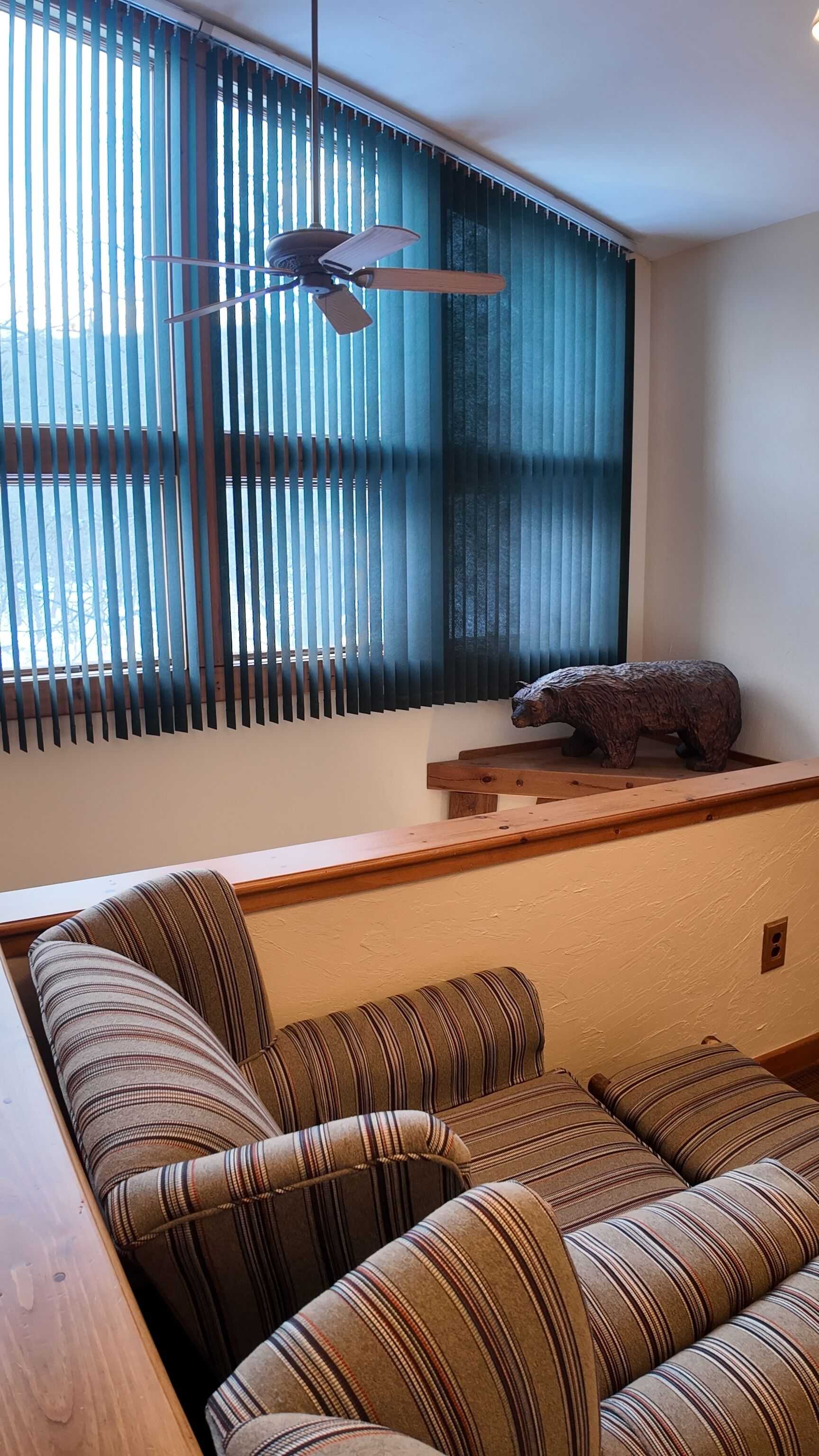 A room with a sofa, a ceiling fan, and a bear statue.