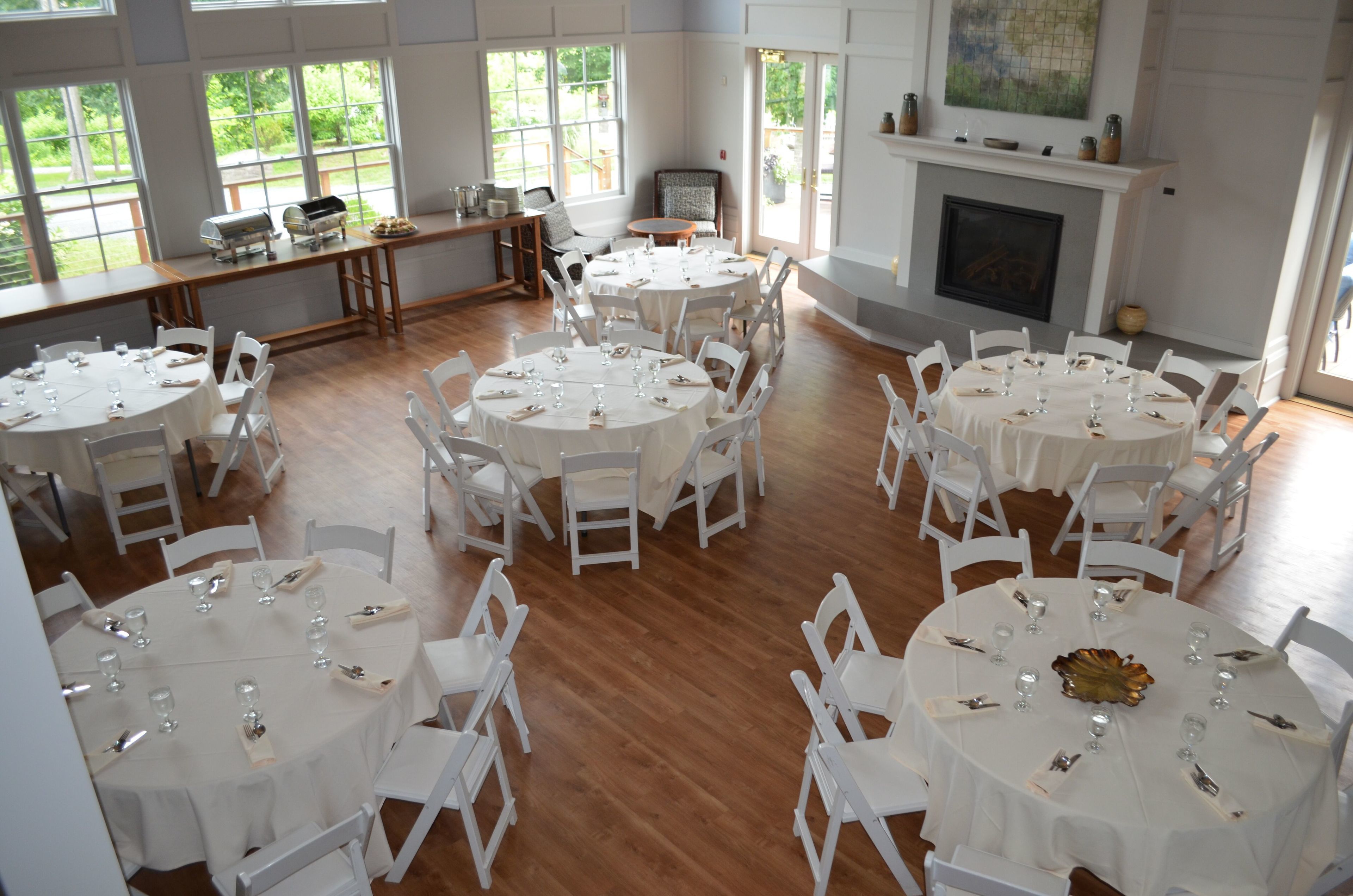 A spacious dining hall with multiple round tables, white chairs, and a fireplace.