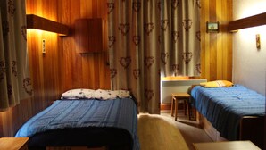 A room with wooden paneling, two beds with blue bedding, a small table, and a wall-mounted heater. - Studio quiet with stunning views over the valley (Montvalezan)
