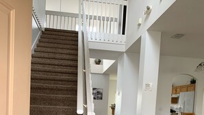 A staircase leading to a second floor with a white railing, a kitchen area with wooden cabinets, and a dining area with chairs. - 5 Bedroom family home in gated community, near Disney. (Davenport)