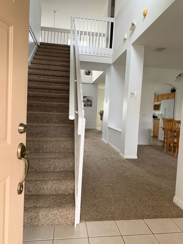 A staircase leading to a second floor with a white railing, a kitchen area with wooden cabinets, and a dining area with chairs.