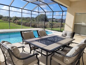A covered patio with a pool, outdoor furniture, and a view of the surrounding landscape.