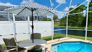 Zona de piscina con área de descanso cubierta, calentador de piscina y vista a un lago.