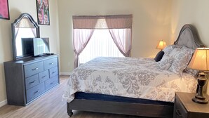 Un dormitorio con cama, cómoda, televisor y cortinas.