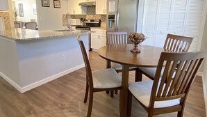 Una cocina moderna con armarios blancos, un refrigerador de acero inoxidable y una mesa de comedor de madera con cuatro sillas.