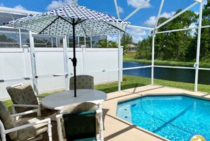 A pool area with a covered seating area, a pool heater, and a view of a lake. - Chic 4-Bedroom Home w/ Pool, Lake View, & Games Room - Minutes from Disney (Kissimmee)