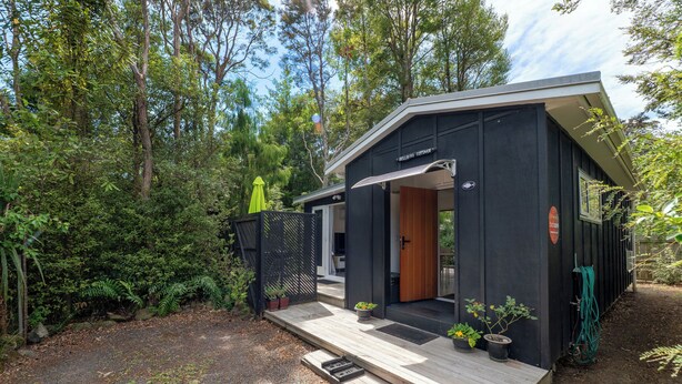 A modern, black cabin-style building with a wooden deck and potted plants.