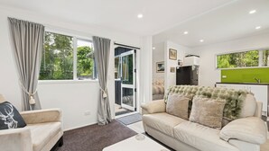 A modern living room with a sofa, a coffee table, and a view of a green garden through a sliding glass door.