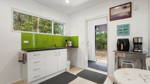 A modern kitchen with white cabinets, a green backsplash, and a window overlooking greenery.
