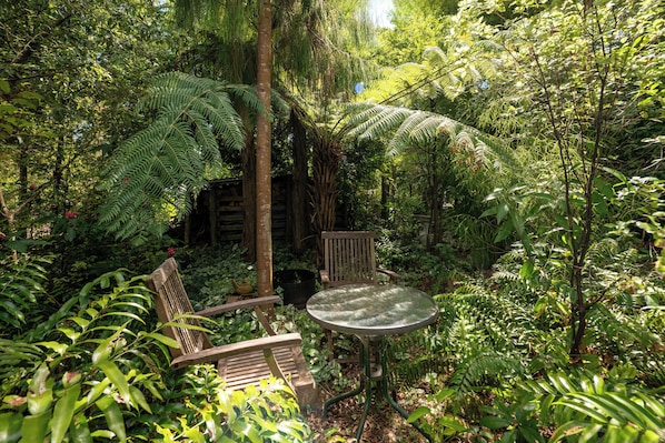 A garden with a wooden bench and a metal table surrounded by lush greenery.