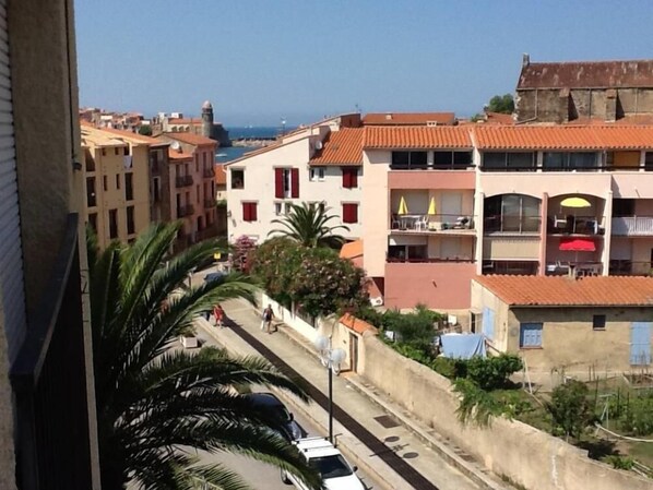 A coastal building with balconies, a street with cars, and palm trees.