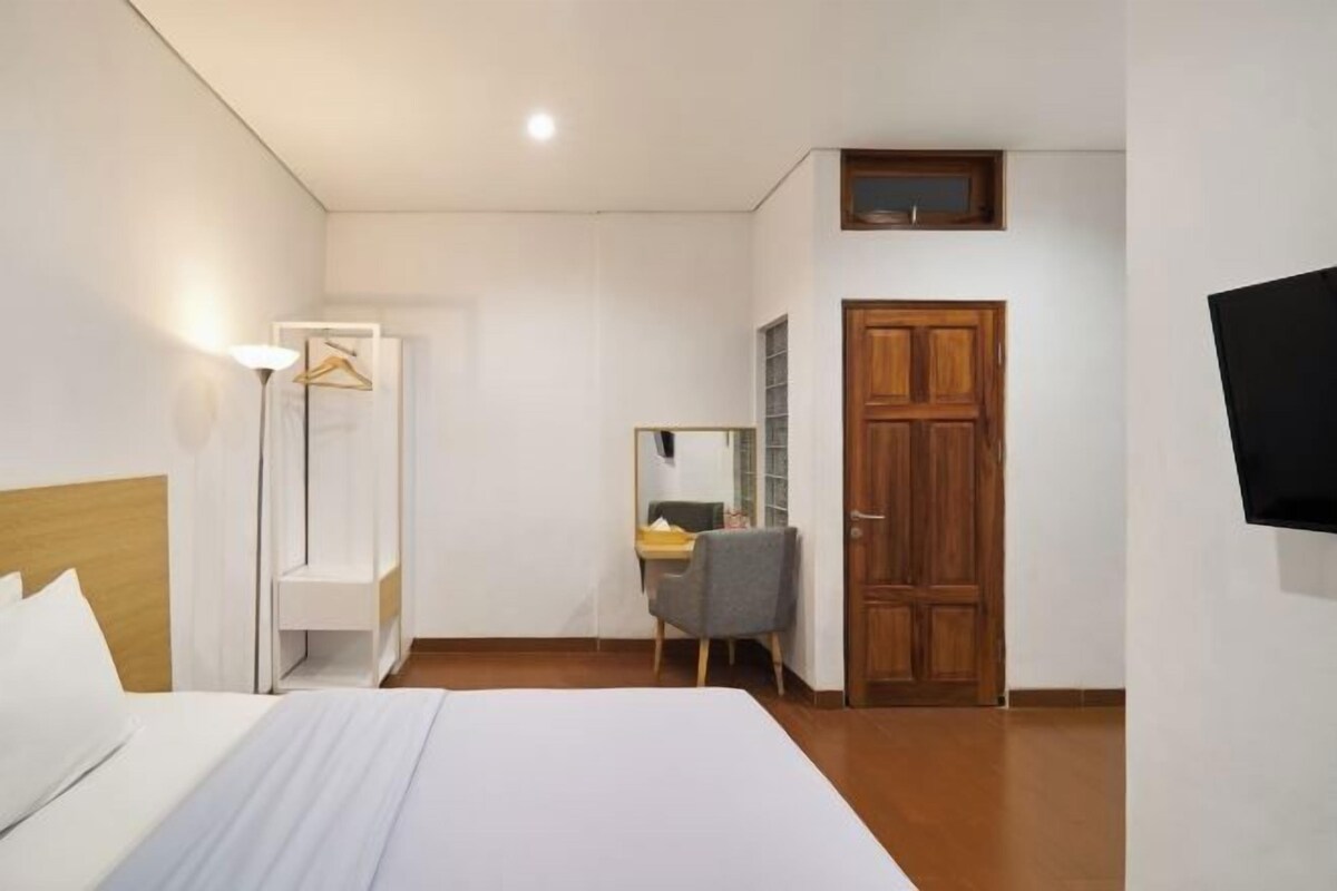 A hotel room with a bed, a desk, a chair, a wardrobe, and a TV mounted on the wall.