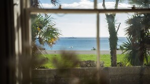 Vista a través de una ventana de una playa con palmeras, un barco y un cielo despejado.