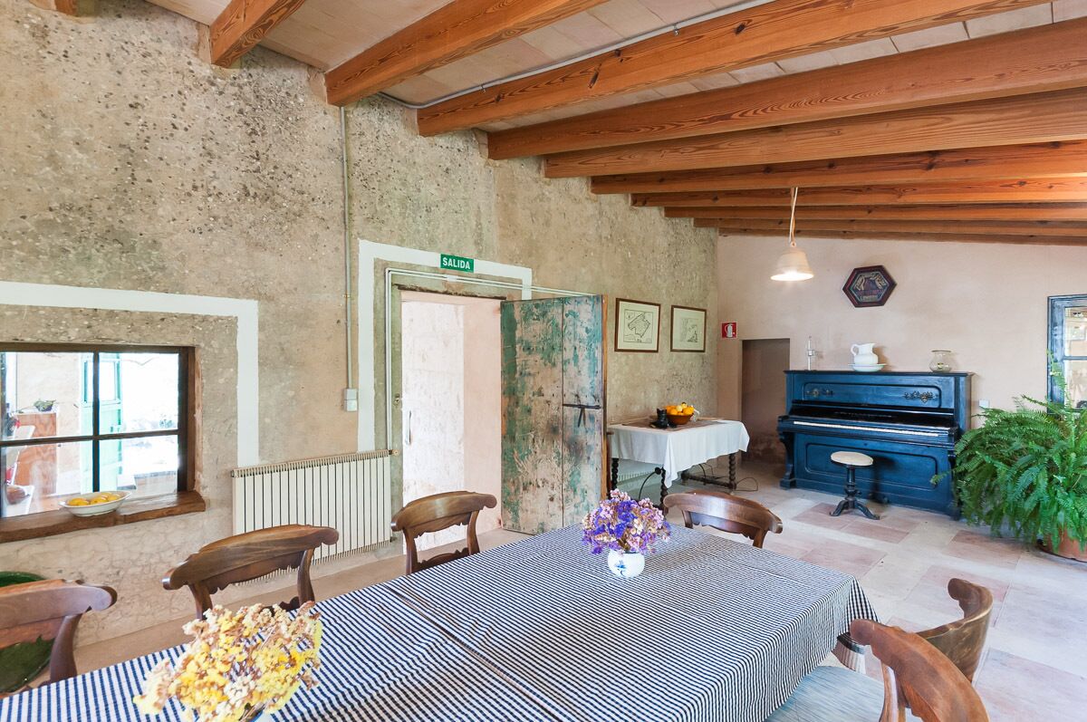 A rustic dining area with a table set for two, wooden chairs, a piano, and a radiator.
