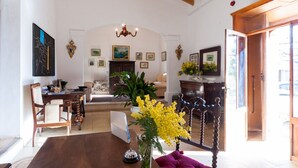 Amplia sala de estar con mesa de comedor de madera, sofá y candelabro. Varias fotografías enmarcadas adornan las paredes y hay una planta en maceta con flores amarillas.