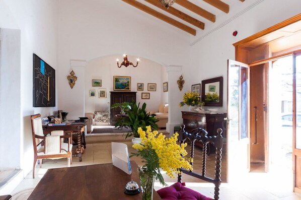 A spacious living room with a wooden dining table, a sofa, and a chandelier. There are several framed pictures on the walls and a potted plant with yellow flowers. - Rural apartment in the center of Mallorca for 2, 4 and 6 people (Sineu)