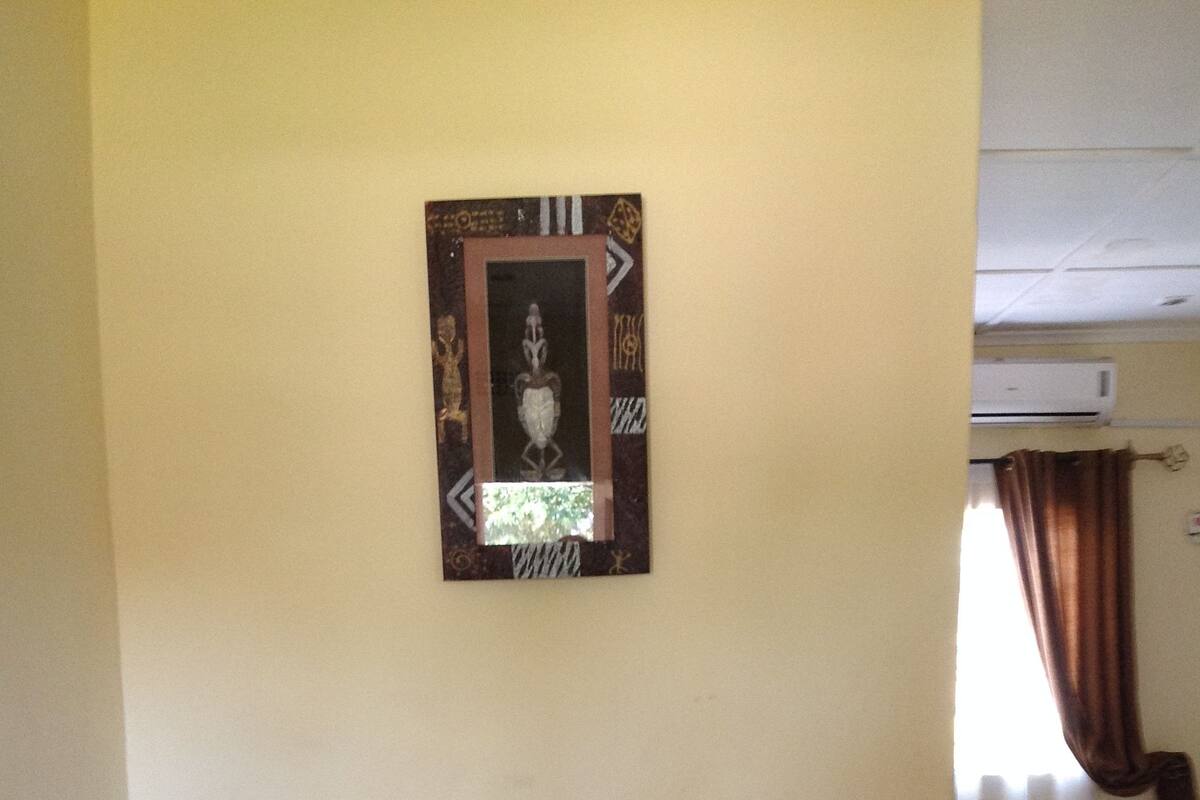 A hallway with a framed artwork on the wall, a trash bin, and a glimpse of a room with a curtain.