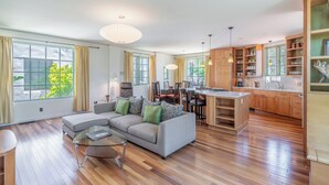 Ein modernes Wohnzimmer mit Ecksofa, Glastisch und Küchenbereich mit Holzausbau und einer zentralen Kochinsel.