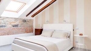 A bedroom with a bed, a small bedside table, a lamp, a round table, and a stone wall. - Lamansarda, romantic place for your holidays. (La Spezia)