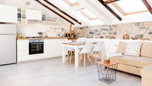 A modern kitchen with a stone wall, a dining area with a wooden table and chairs, and a cozy seating area with a sofa and a small coffee table. - Lamansarda, romantic place for your holidays. (La Spezia)