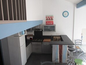 Cozinha compacta com micro-ondas, fogão e pia. Há um letreiro da Coca-Cola na parede e um relógio.