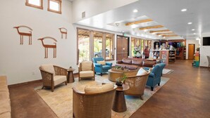 A spacious lobby with a variety of seating options, including sofas and armchairs, a coffee table, and a rug. There are wooden wall decorations and a large window allowing natural light.