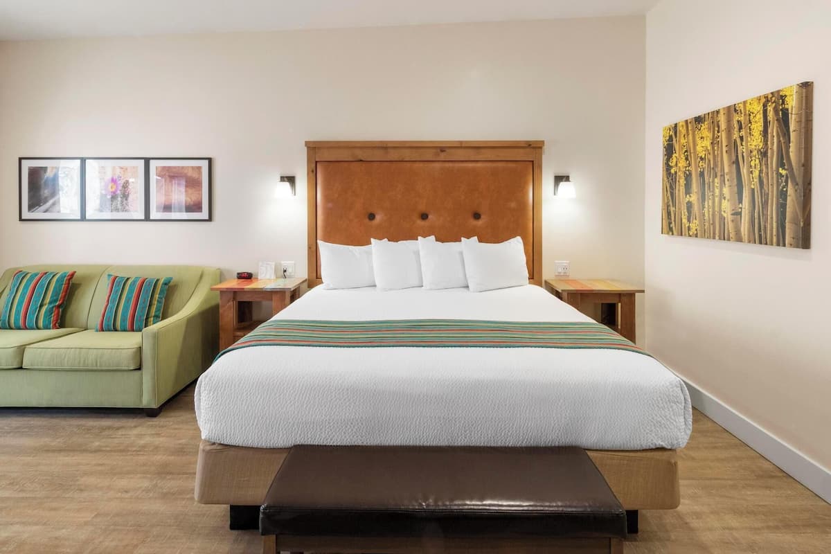 Een hotelkamer met een groot bed, een groene bank, een houten bankje en een muur met drie ingelijste foto's.