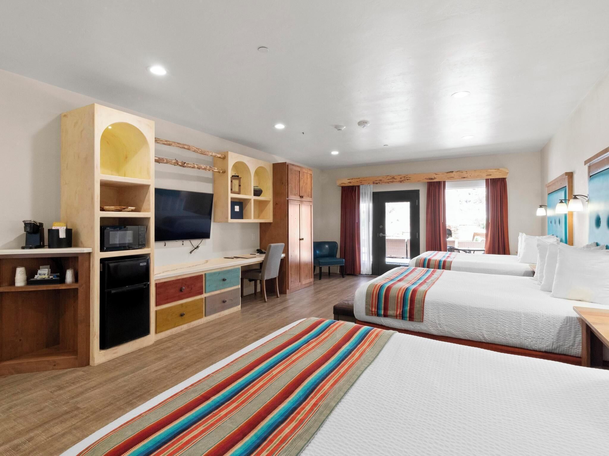 A hotel room with two beds, a desk with a computer, a television, and a small seating area.